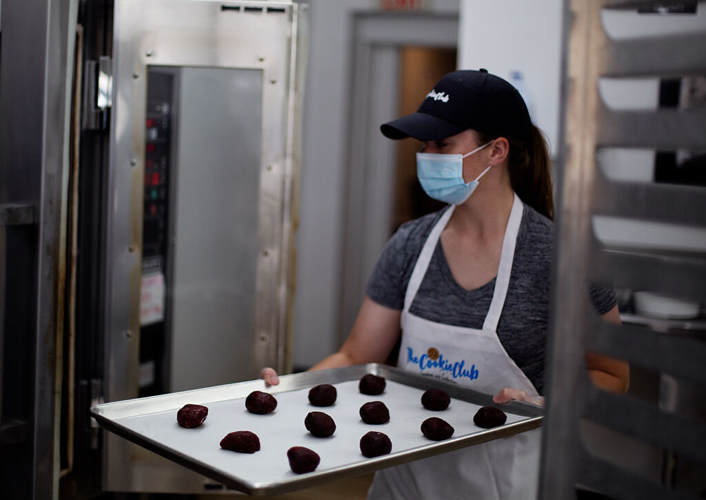 Belle Graves carries a sheet of unbaked cookies through the Cookie Club kitchen